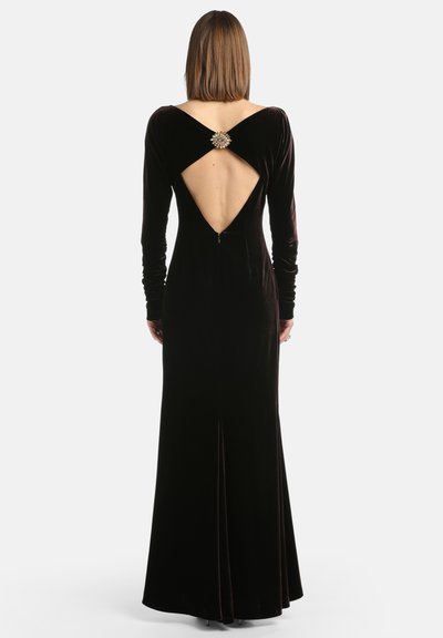 Ilga juoda aksomo suknelė su ilgomis rankovėmis, iškirpimu nugaroje ir dekoratyvine segtuku kaklo srityje. tiesus siluetas su įpjova.