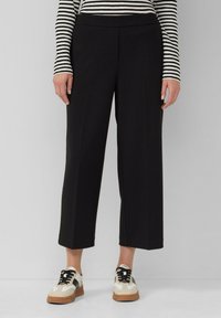 Zwarte wijde broek met een gladde textuur, middelhoge tailleband, gecombineerd met crèmekleurige en bruine sneakers met zwarte veters.
