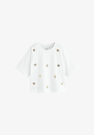 Chemise blanche à manches courtes avec col rond, décorée de petits motifs floraux brodés en or et argent éparpillés sur le devant.