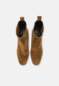 Bottines en suede marron avec un design épuré, des bouts pointus et un revêtement texturé sur les côtés. Dispose d'une languette pour un enfilage facile.