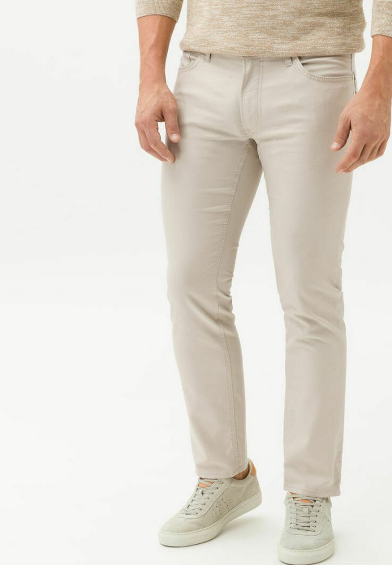 Beige slim-fit chinos made of cotton blend, featuring front and back pockets, and accompanied by light gray sneakers.
