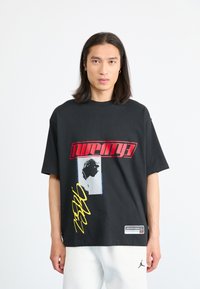 Black t-shirt with short sleeves featuring bold red and yellow graphics, a portrait silhouette, and a “Jordan” logo tag on the hem.