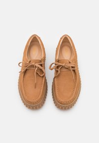 Chaussures en cuir marron clair avec une finition texturée, bout rond et semelle en caoutchouc. Elles présentent un design à lacets et des accents de couture minimalistes.
