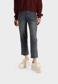 Jeans di denim in un blu sbiadito, accorciati con orli sfrangiati, abbinati a sneaker platform beige. Indossati con una felpa bordeaux.