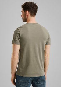 Camiseta de algodón verde oliva con cuello redondo y mangas cortas, que presenta una textura suave y un corte regular. La vista trasera muestra un diseño simple.