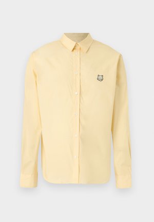 Pale yellow long-sleeve button-up shirt with collar and small embroidered wolf head on left chest.