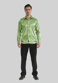Chemise en satin vert à boutons avec manches longues, portée par un homme en pantalon et chaussures noirs, sur fond neutre.