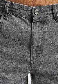 Harmaat farkut sisältävät klassisen muotoilun, metallinappisuljenta, vyölenkit ja hienovaraisesti strukturoidun kankaan.