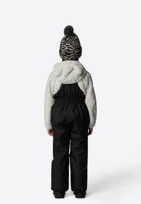 Black snowsuit with a fluffy white hooded top. The hood features bear ears. Patterned black and white knit hat with pompom on top.