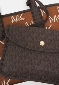 Brun og mørkebrun Michael Kors håndtaske og matchende pung med et all-over MK logo mønster og detaljer i guldtonet hardware.