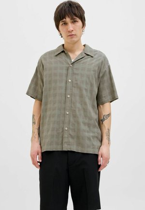Camisa de manga corta color verde olivo con un sutil patrón a cuadros, cierre de botones al frente y un corte holgado. Textura suave, diseño de cuello clásico.