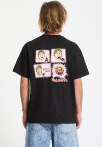 Camiseta de algodón negra con ilustraciones gráficas de dibujos animados en rosa, con un personaje rojo y el texto "VOLCOM" en la parte posterior. Corte relajado.