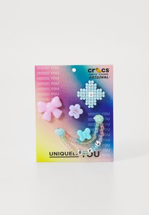 Charms Jibbitz colorés pour Crocs, y compris un noeud rose, une fleur bleue et un design en perles écrivant "BFF", présentés sur un fond dégradé.