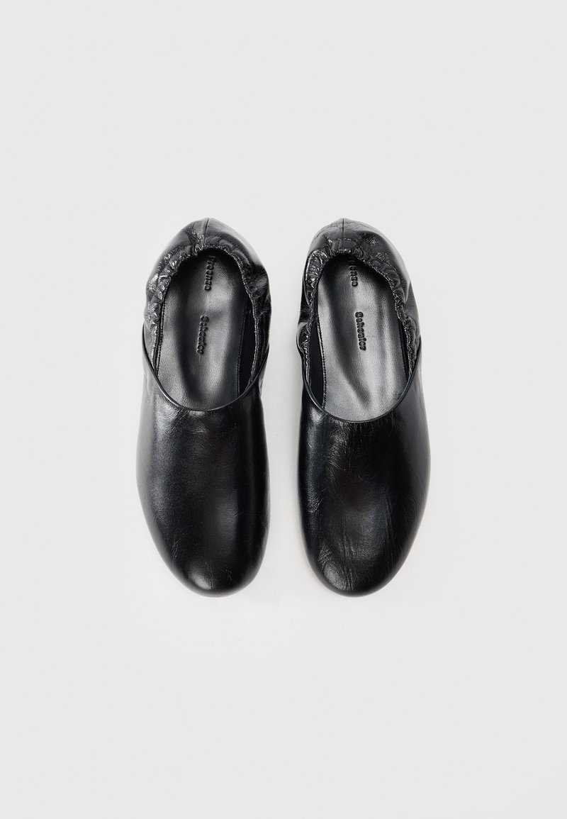 Black leather slip-on shoes featuring a rounded toe, elasticized edge, and smooth surface texture. Interior has subtle branding details.