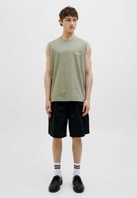 Sømløs olivengrønn bomulds skjorte med gult logo, parret med sorte cargo shorts, sorte sko og hvide sokker med sorte striber.