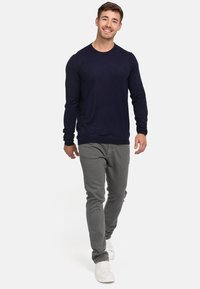 Camisa de manga larga azul marino hecha de tela suave, combinada con pantalones ajustados gris claro y zapatillas blancas. Modelo de pie caminando hacia adelante.