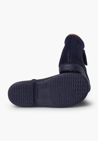 Botines de ante azul marino con suela de goma texturizada, que cuentan con un zipper lateral y un acento de cuero marrón en el talón.