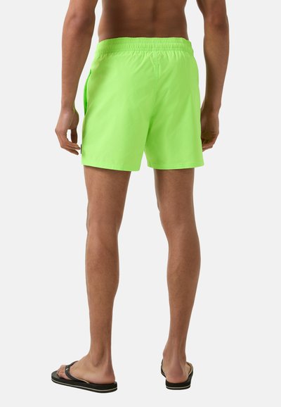 Neonově zelené plavky vyrobené z lehkého materiálu, s elastickým pasem a bočními kapsami, stylizované s uvolněným střihem.