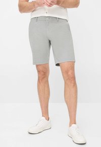 Pantaloni corti grigi, fino al ginocchio, realizzati in tessuto texturizzato con chiusura a bottone e passanti per cintura, abbinati a sneakers bianche.