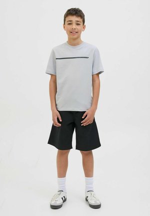 Grå t-shirt med korte ærmer og en sort vandret stribe, parret med sorte shorts. Hvide ankelstrømper og sportssko med sorte accenter.