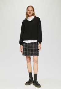 Czarny sweter w serek z puffowanymi rękawami nałożony na białą koszulę z kołnierzykiem, zestawiony z czarno-białą spódnicą w kratę z tweedu i masywnymi czarnymi botkami.