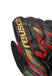 Schwarzer Fußballhandschuh mit goldenem "reusch"-Logo, roten und goldenen geometrischen Mustern, strukturierter Oberfläche und schwarzem Netz-Handgelenk für Atmungsaktivität.