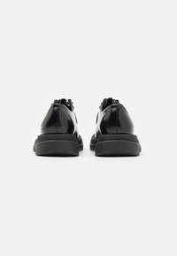 Black patent leather shoes with a smooth finish, featuring a contrasting black textured rubber sole and minimalistic design.