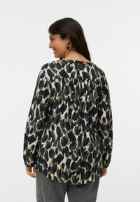 Blouse à manches longues avec un design imprimé léopard, présentant des nuances de noir, vert et beige, avec un détail froncé au dos et une texture douce.