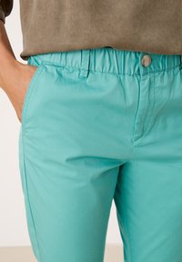 Turkosa byxor med resårmidja, knäppning fram, slät textur och sidfickor. Inga synliga mönster eller detaljer.