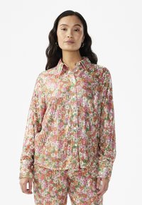 Cămașă strălucitoare, cu paiete, în modele florale cu nuanțe de roz, verde și aur. Prezintă un guler și închidere cu nasturi. Mâneci lungi.