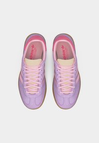 Dvojice tenisek Adidas v růžové a lila barvě s béžovým jazykem a gumovou podrážkou, pohled shora na bílém pozadí.