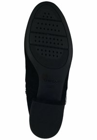 Suela de zapato de ante negro con una superficie de goma con patrón que presenta orificios circulares para transpirabilidad. Incluye la marca "GEOX" en relieve.