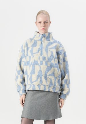 Fleece pullover in lichtblauw en roomkleur met geometrische patronen; heeft een hoge kraag en een halve rits; zachte textuur; oversized pasvorm.