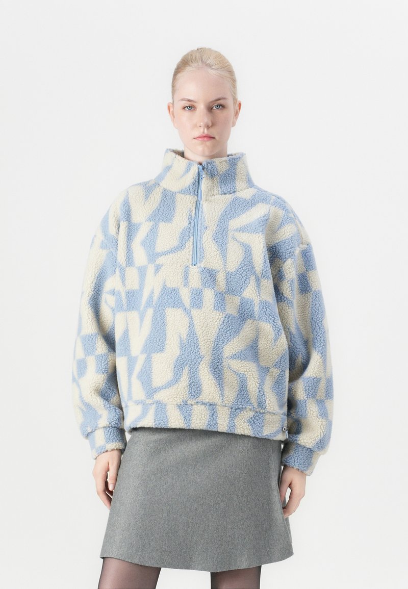 Fleece pullover in lichtblauw en roomkleur met geometrische patronen; heeft een hoge kraag en een halve rits; zachte textuur; oversized pasvorm.