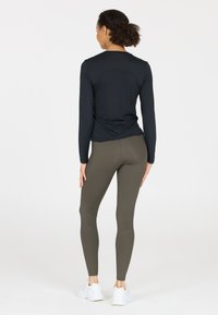 Zwarte longsleeve shirt en olijfgroene leggings met geribbelde accenten, gecombineerd met witte sneakers. Glad materiaal, slim-fit ontwerp.