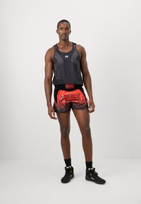 Sort ærmeløs tank top med mesh detaljer, rød og sort gradient shorts med "RULS" logo, sorte sportsko med grønne accenter.