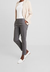 Beige blazer över en vit topp, kombinerad med grå rutiga byxor och vita platta skor. Fokusera på skräddarsydd passform och släta texturer.