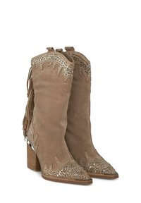 Bottes en daim marron, hautes jusqu'au genou, avec des franges, des pointes effilées et des embellissements métalliques sur le dessus et les côtés. Talons carrés en bois.