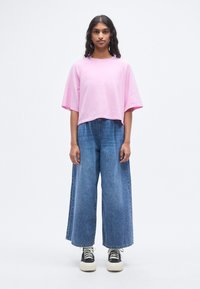 T-shirt en coton rose surdimensionné à manches courtes, associé à un pantalon en denim bleu clair à jambes larges et des baskets noires à semelles blanches.