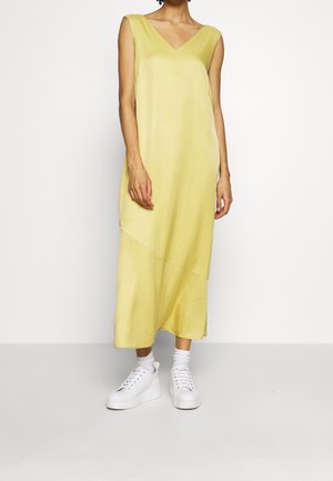 Femme portant une robe midi jaune sans manches associée à des chaussettes blanches et des baskets à plateforme blanches, debout sur un fond uni.