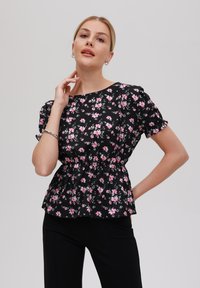 Svart blommig blus med korta puffärmar, med en åtdragen midja och spridda rosa blommor. Lätt tyg med en mjuk textur.