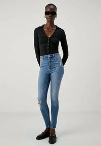 Μαύρο πουκάμισο με μακριά μανίκια και κουμπιά, μπλε ψηλόμεσο Skinny τζιν με φθαρμένες λεπτομέρειες και μαύρες επίπεδες loafers.