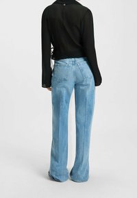 Chemise noire semi-transparente à manches longues avec boutons et taille cintrée, associée à un jean en denim bleu clair à jambes larges avec poches arrière.