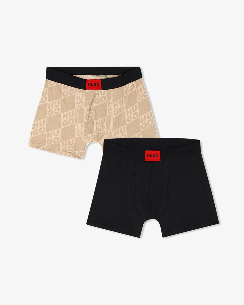 Δύο ζευγάρια ανδρικά μπόξερ, ένα μπεζ με επαναλαμβανόμενο κείμενο "HUGO" και ένα μονόχρωμο μαύρο, και τα δύο με μαύρες ζώνες μέσης και κόκκινες ετικέτες "HUGO".