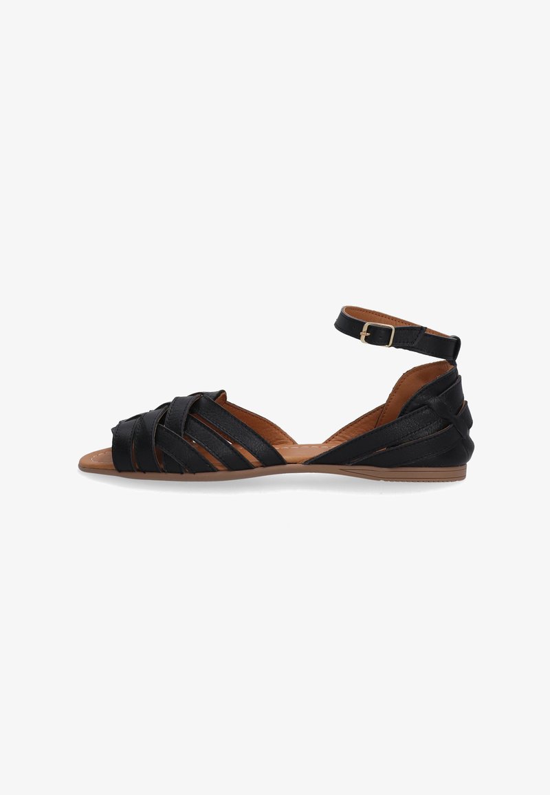 Sort lædersandal med krydstræk, ankelrem med spænde, flad sål og tan-farvet indersål. Glat tekstur og minimalistisk design.