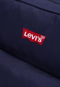 Navy blue fabric with a textured surface featuring a prominent red embroidered Levi's logo in a classic design.