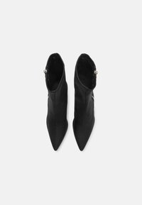 Botas de cuero negro hasta el tobillo con puntas afiladas, cierre con cremallera en un lado y textura suave. Los detalles de costura añaden estructura.