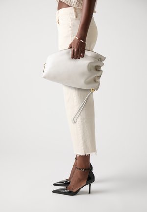 Clutch de cuero blanco con diseño recogido, detalle de cremallera dorada, sostenido por una persona que lleva pantalones cortos marfil y tacones negros de punta.