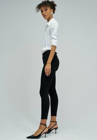 Jeans skinny negros combinados con una camisa blanca de botones y tacones negros de punta. Presenta un diseño ajustado con mangas remangadas.