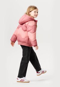 Rosa Puffjacke mit Chevron-Muster, Kapuze, gerippten Bündchen und Saum, kombiniert mit schwarzen Jeans und weißen Sneakers mit roten Streifen.